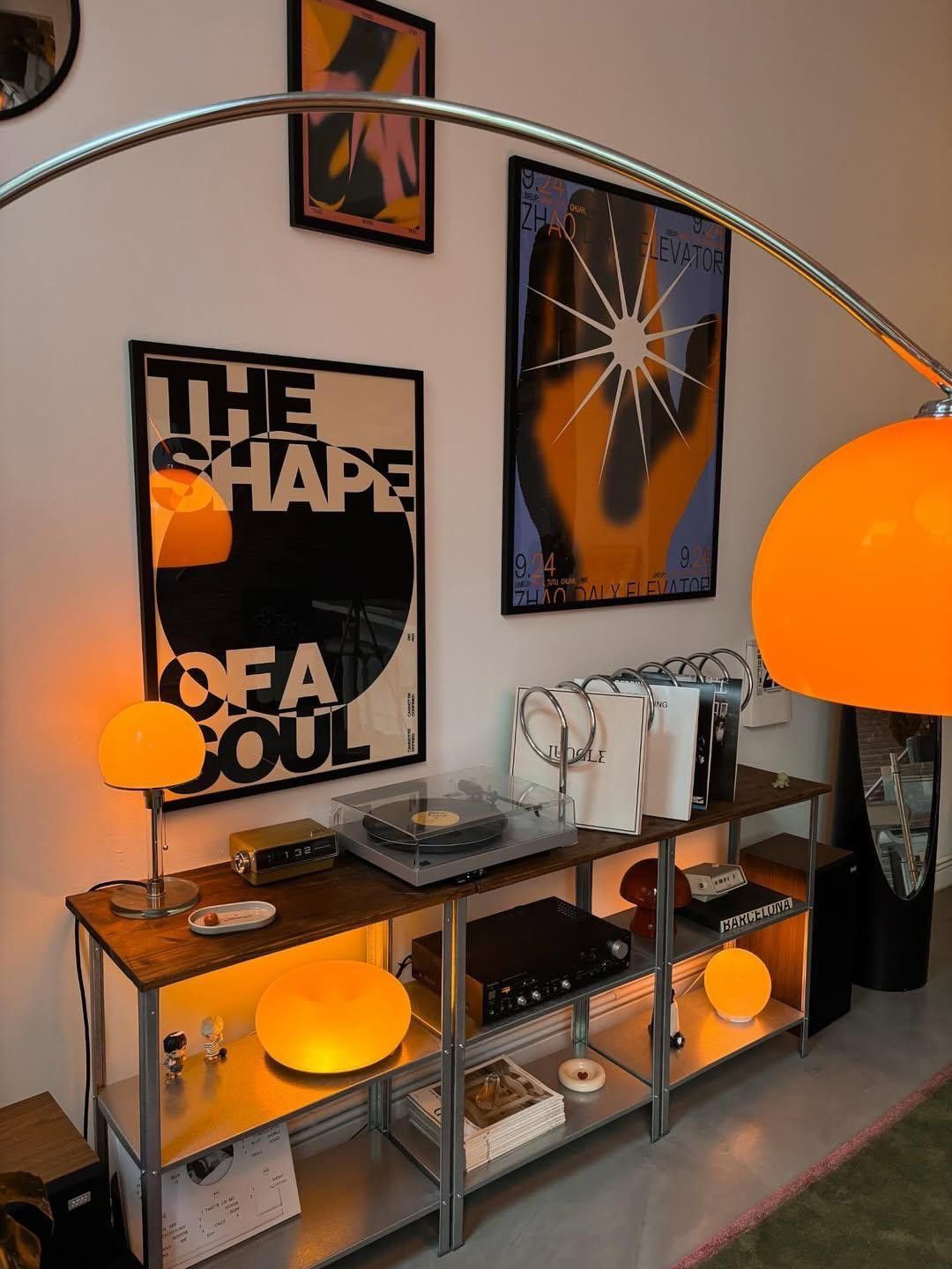 Orange arc lamp above a chrome and wood record cabinet with graphic posters