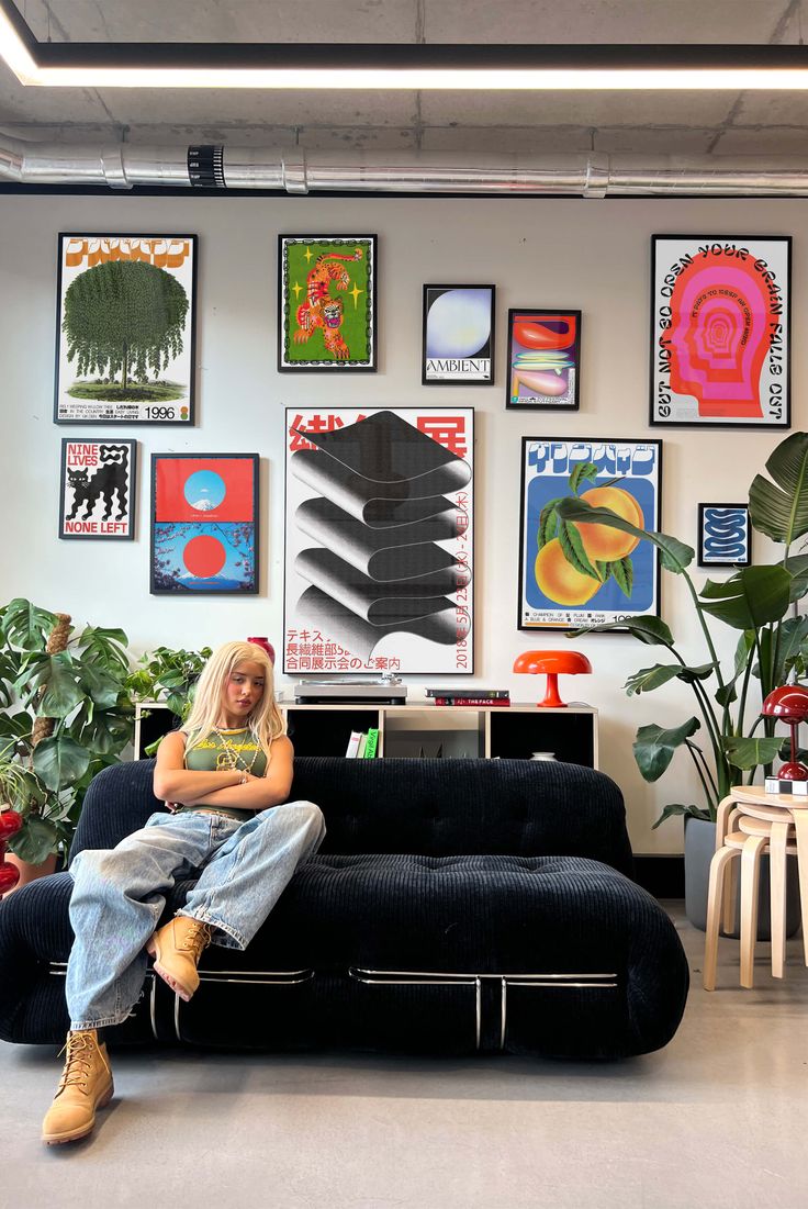 Black sofa beneath a colorful gallery wall with plants and orange lamps